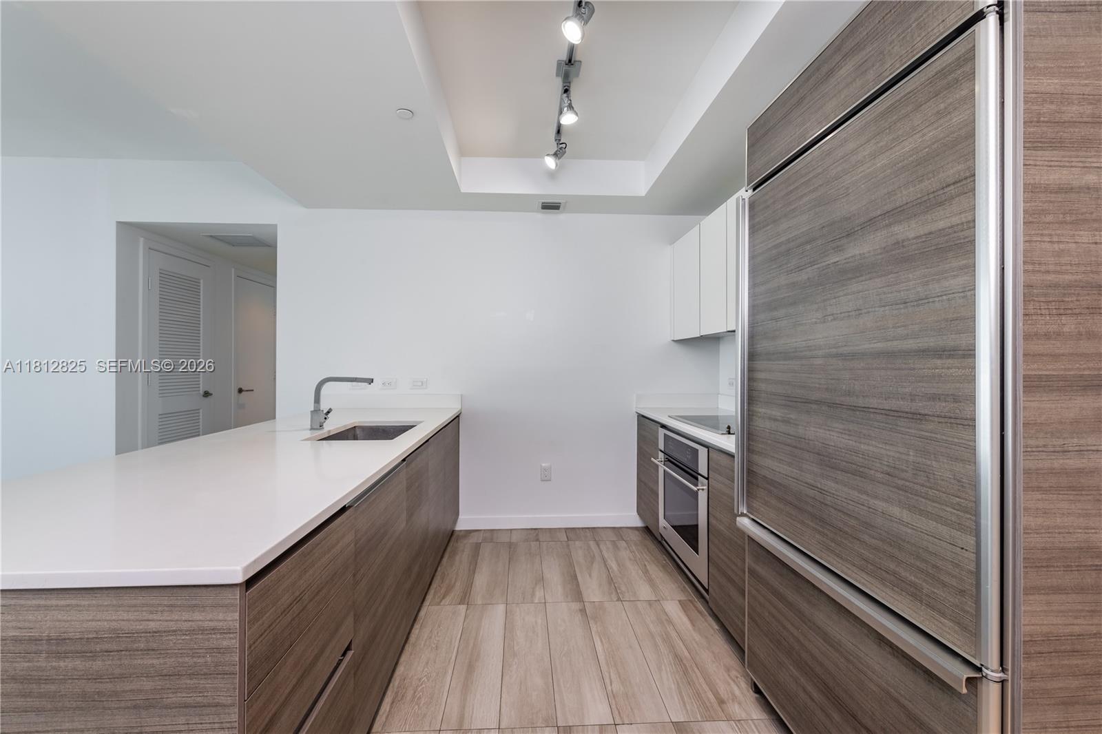 A modern kitchen features wood-grain cabinetry, white countertops, stainless steel appliances, and recessed lighting — 1100 S Miami Ave # 1704, Miami FL 33130, MIAMI, FL