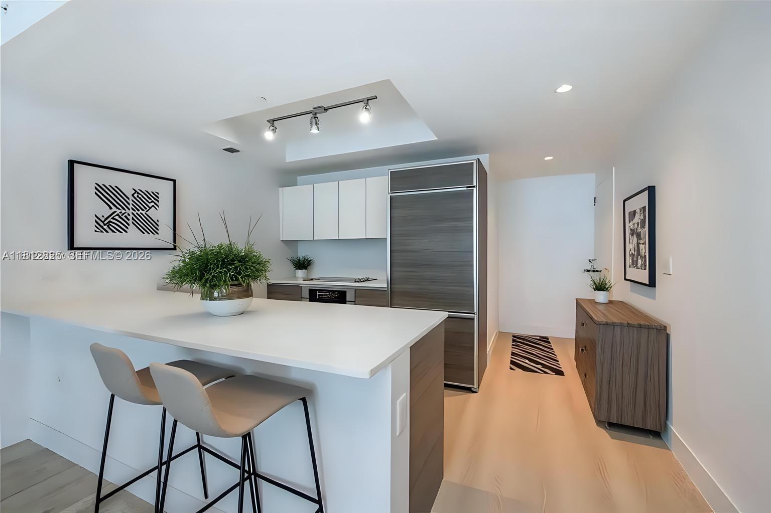 A modern kitchen features white countertops, two bar stools, and wood-toned cabinetry — 1100 S Miami Ave # 1704, Miami FL 33130, MIAMI, FL