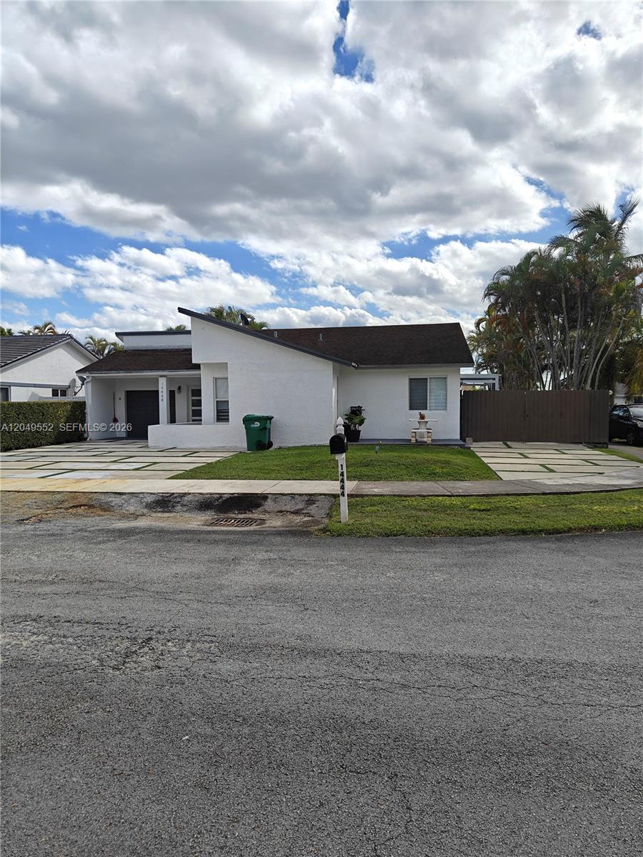 A single-story white house features a modern roofline, a paved driveway, and a green lawn — 14444 SW 107th Ter, Miami FL 33186, MIAMI, FL
