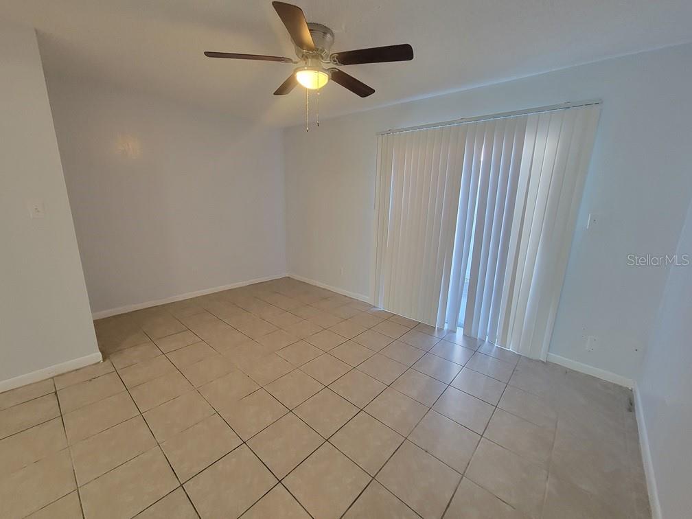 An empty room features light-colored tile flooring, a ceiling fan, and vertical sliding glass doors — 5122 TEMPLE HEIGHTS ROAD UNIT D, TAMPA, FL