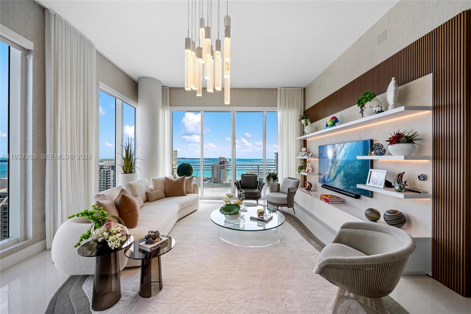 A modern living room features a curved sofa, glass coffee table, and floor-to-ceiling ocean views — 900 Brickell Key Blvd # 2004, Miami FL 33131, MIAMI, FL