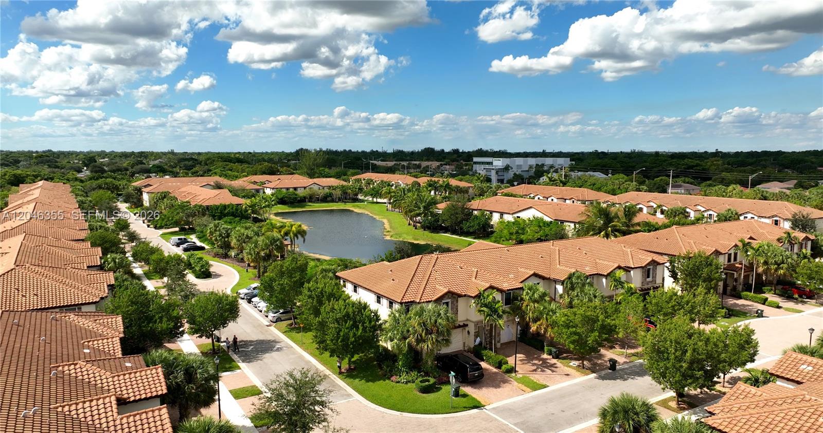 An aerial view shows a residential community with tile-roofed townhomes surrounding a central pond — 3962 Devenshire Ct, Coconut Creek FL 33073, COCONUT CREEK, FL