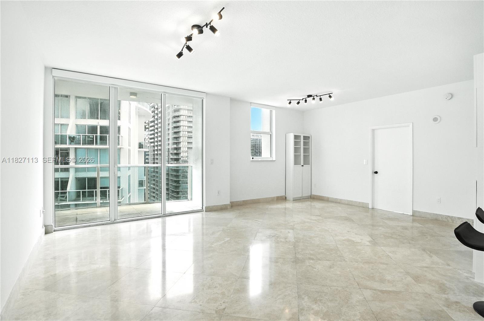 A bright, empty room features white walls, marble tile flooring, track lighting, and a balcony — 31 SE 5th St # 4021, Miami FL 33131, MIAMI, FL