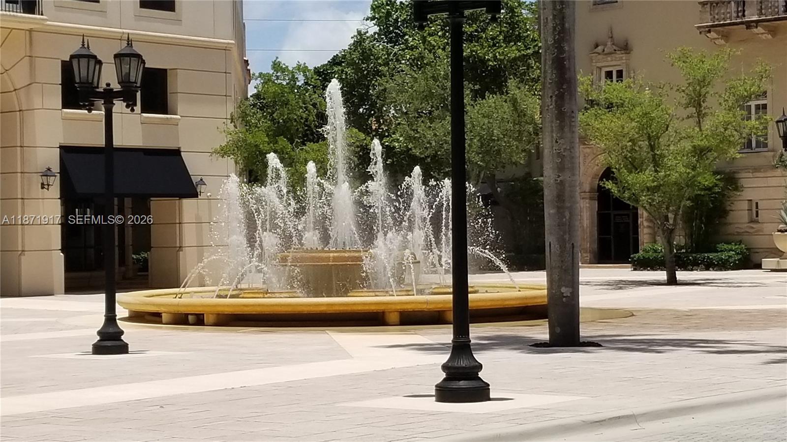 A tiered stone fountain sits in a paved plaza between two buildings with street lamps — 888 S Douglas Rd # 1213, Coral Gables FL 33134, CORAL GABLES, FL