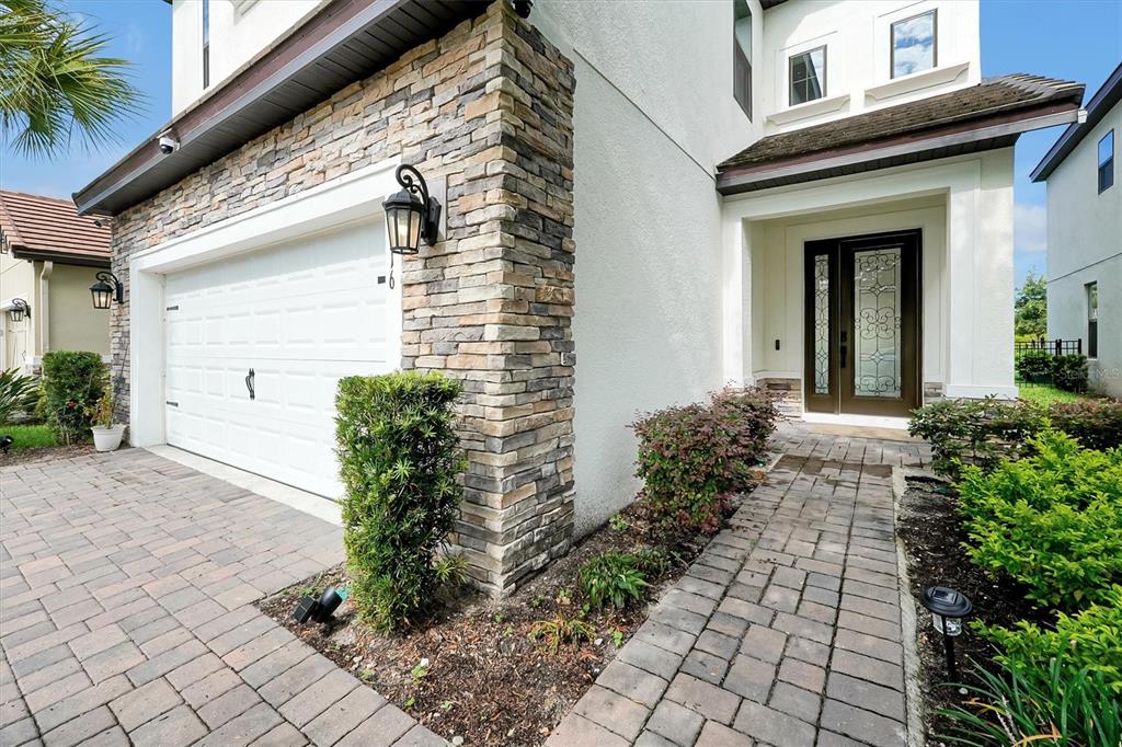 A stone-accented house exterior features a white garage door, a paved walkway, and front door — 1316 BLUE STEM LANE, WINTER PARK, FL