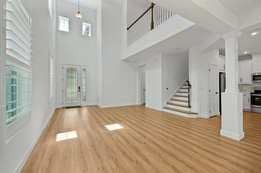 A bright, high-ceilinged entryway features light wood-look flooring, a staircase, and a front door — 1316 BLUE STEM LANE, WINTER PARK, FL