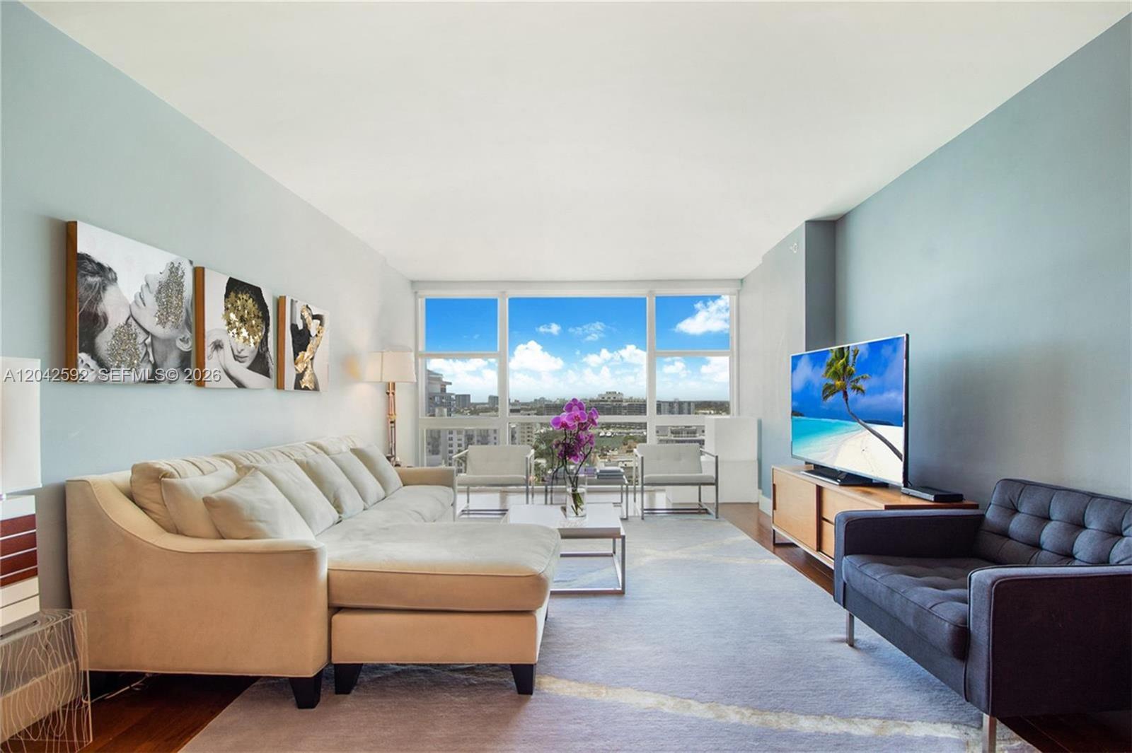 A living room features a sectional sofa, a dark armchair, and large floor-to-ceiling windows — 6801 Collins Ave # 1101, Miami Beach FL 33141, MIAMI BEACH, FL