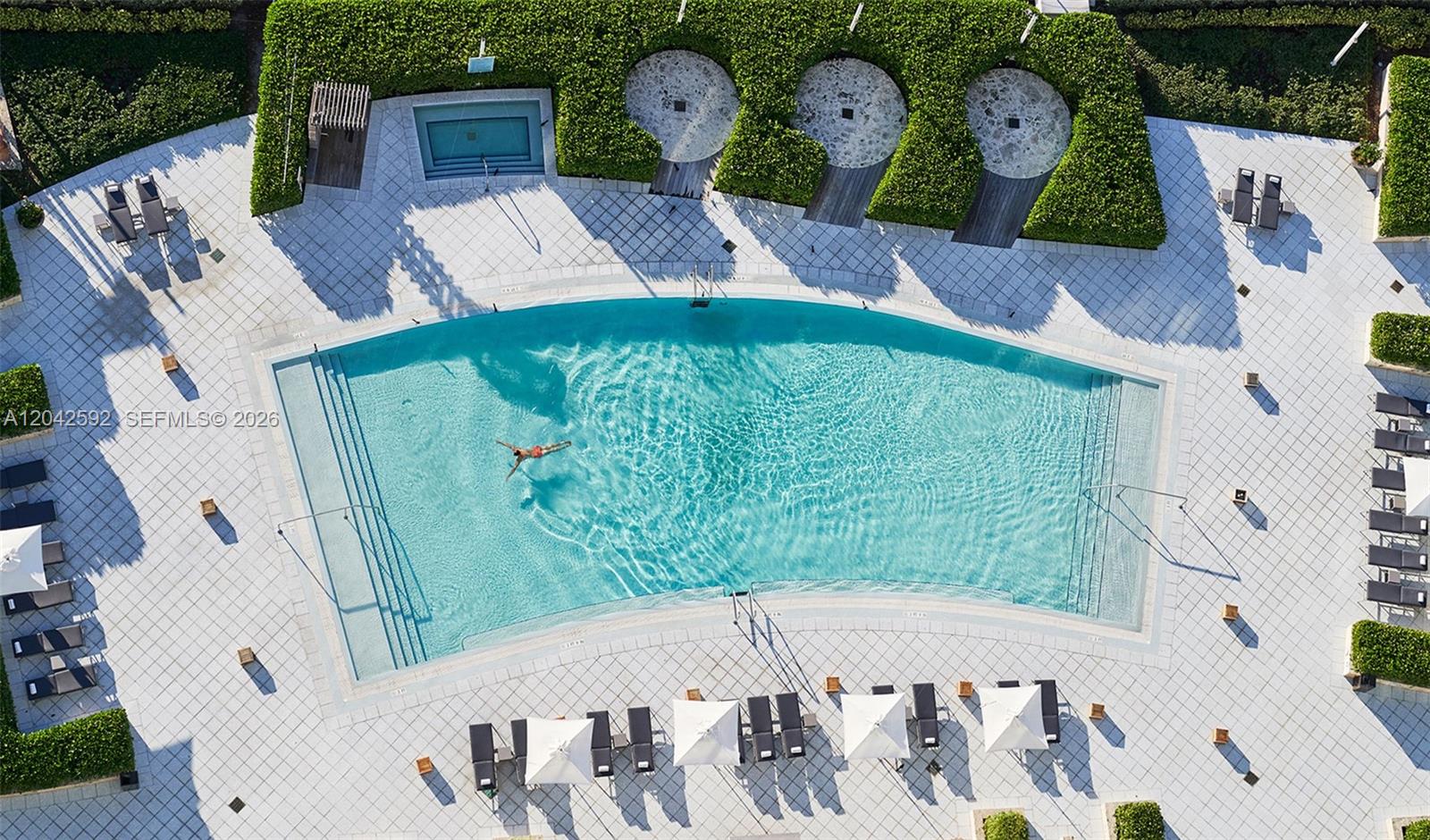 An aerial view shows a swimming pool with a person swimming and surrounding lounge chairs — 6801 Collins Ave # 1101, Miami Beach FL 33141, MIAMI BEACH, FL