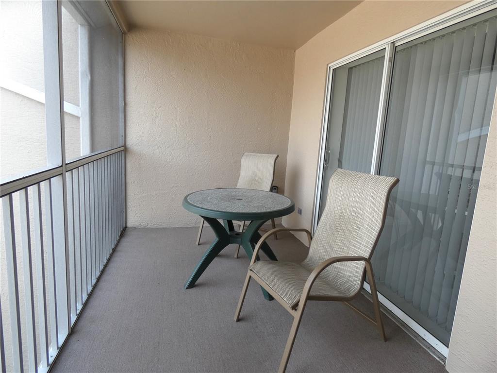 A screened-in balcony features a small round table and two chairs on a concrete floor — 9641 CASTLE POINT DRIVE UNIT 1225, SARASOTA, FL