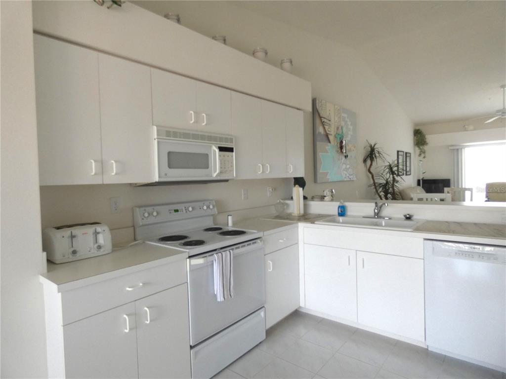 A white kitchen features white cabinetry, a white stove, a dishwasher, and a double sink — 9641 CASTLE POINT DRIVE UNIT 1225, SARASOTA, FL