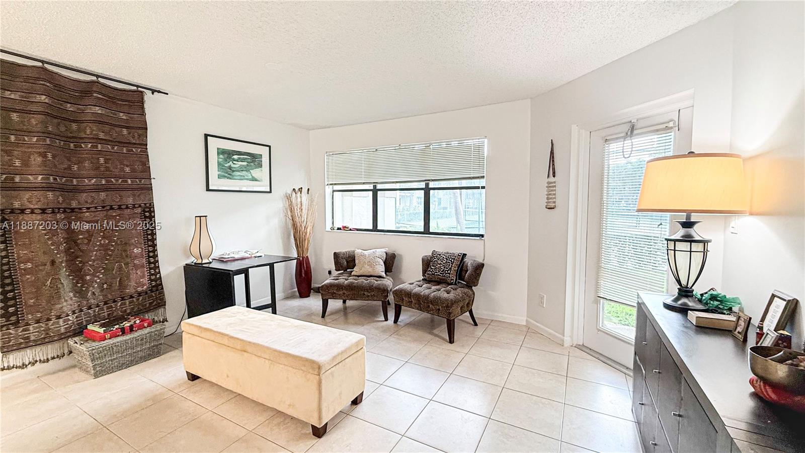 A living room features tiled floors, two armchairs, a storage ottoman, and a glass door — 540 S Park Rd # 9, Hollywood FL 33021, HOLLYWOOD, FL