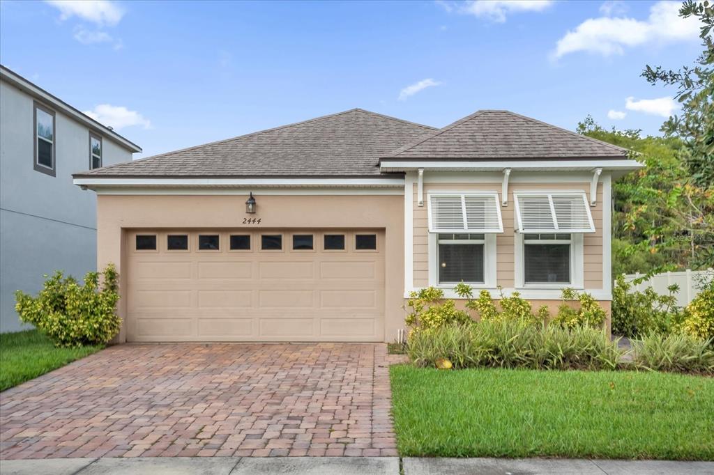A single-story house with a beige stucco exterior, a two-car garage, and a brick driveway — 2444 VARENNA LOOP, KISSIMMEE, FL