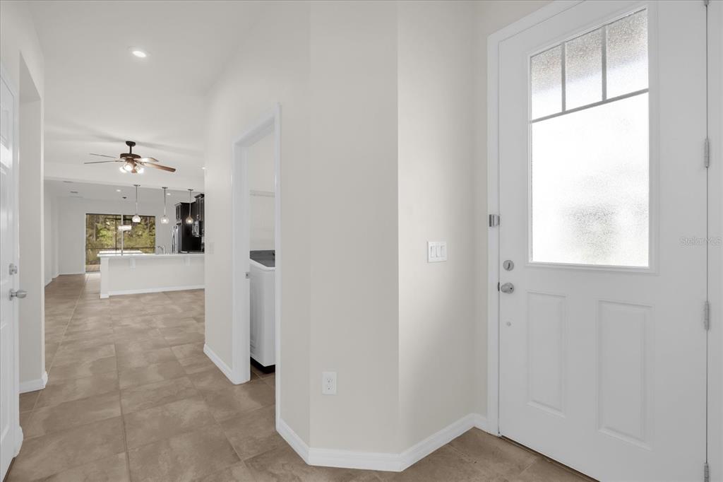 An entryway with a white front door leads to a tiled hallway and open kitchen — 2444 VARENNA LOOP, KISSIMMEE, FL