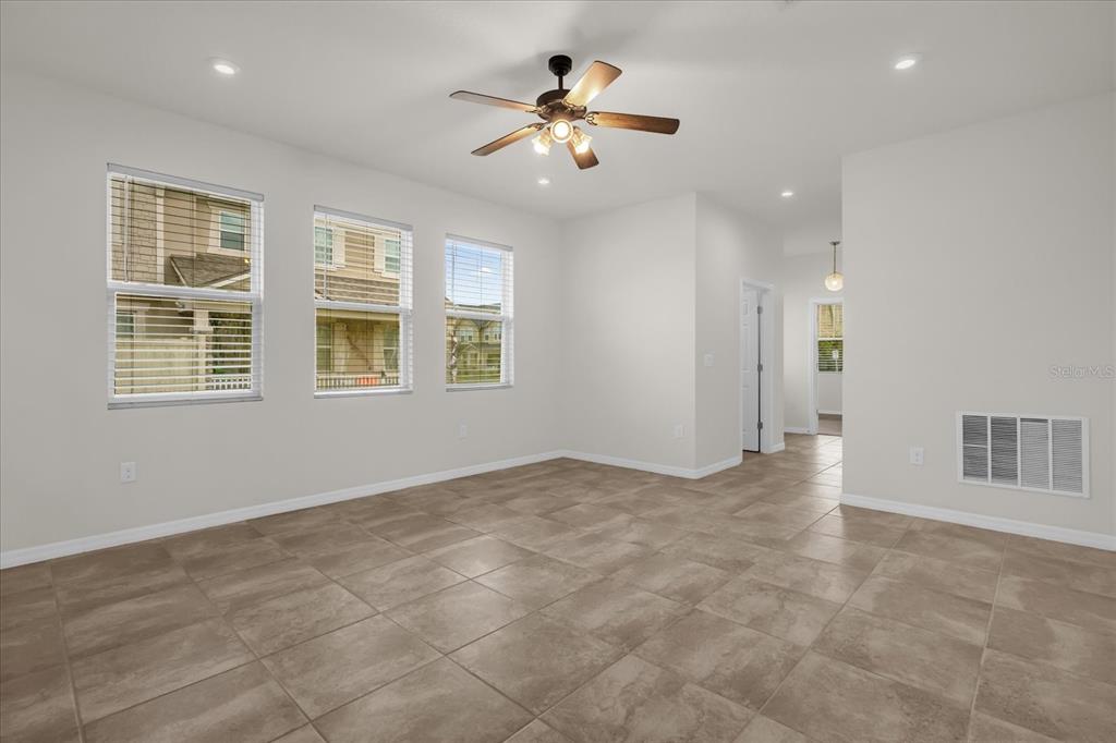 A bright, empty room features light tile flooring, three windows, and a ceiling fan — 2444 VARENNA LOOP, KISSIMMEE, FL