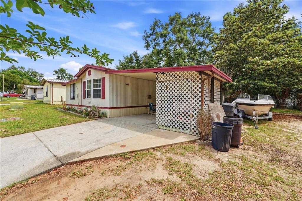 A mobile home with a carport, lattice enclosure, and a boat parked on the side — 1908 REGINA DRIVE, LAKE ALFRED, FL
