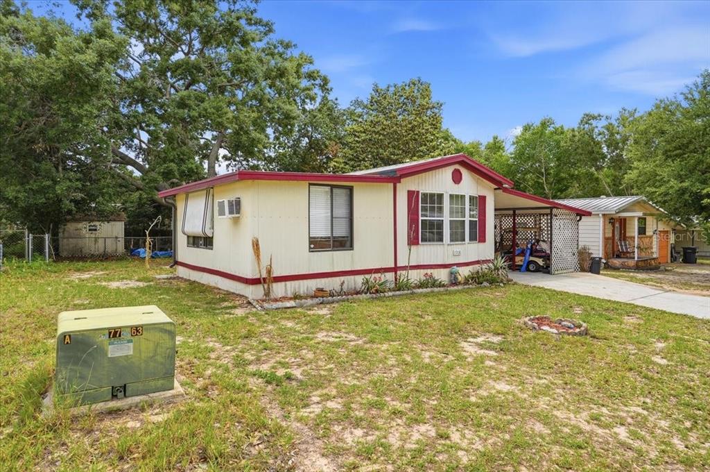 A single-story mobile home with a carport sits on a grassy lot with trees — 1908 REGINA DRIVE, LAKE ALFRED, FL