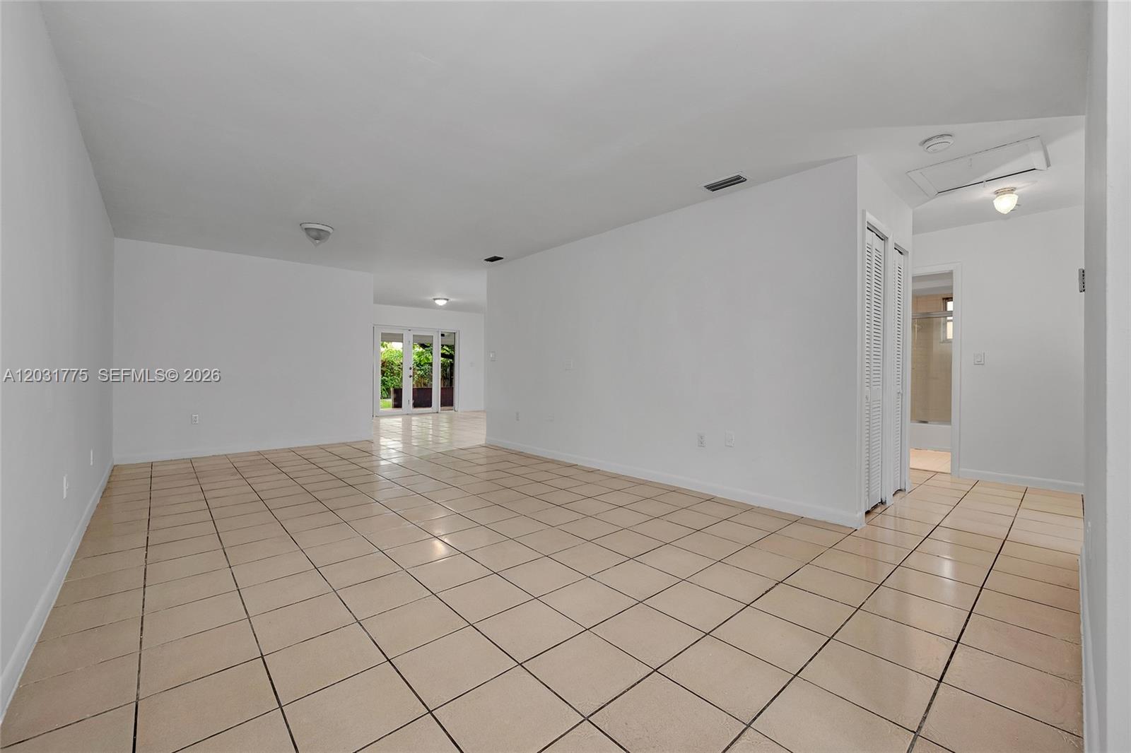 An empty room with white walls, beige tile flooring, and a doorway leading outside — 23 NW 109th Ave, Miami FL 33172, MIAMI, FL
