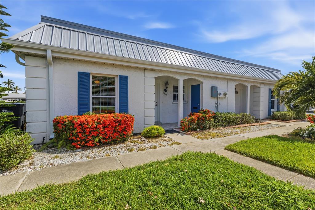 A single-story white stucco building with a metal roof and blue shutters — 9821 HERNANDO COURT, BRADENTON, FL