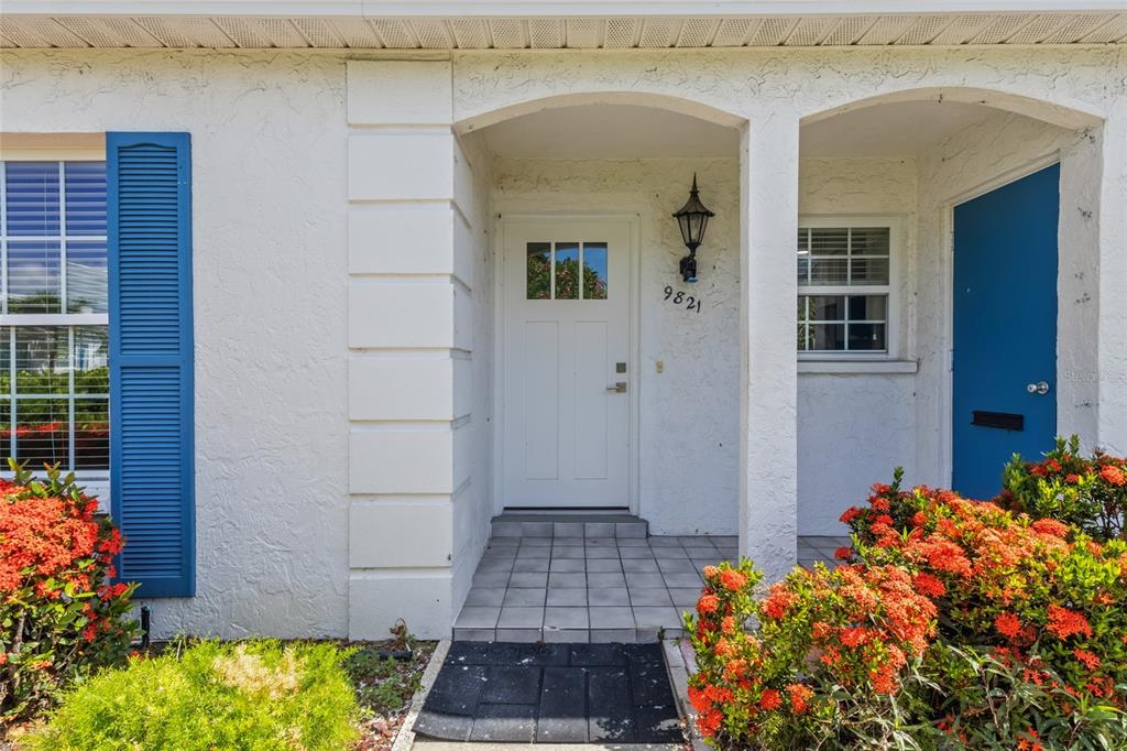 The exterior of a home features a white front door, blue shutters, and red flowers — 9821 HERNANDO COURT, BRADENTON, FL