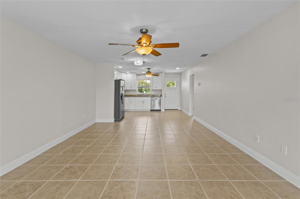 An open-concept room features light tile flooring, white kitchen cabinetry, and two ceiling fans — 9821 HERNANDO COURT, BRADENTON, FL