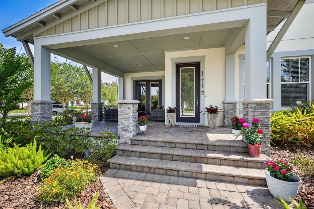 A covered front porch with stone pillars, brick steps, and potted flowers leads to a door — 13201 GRANGER AVENUE, ORLANDO, FL
