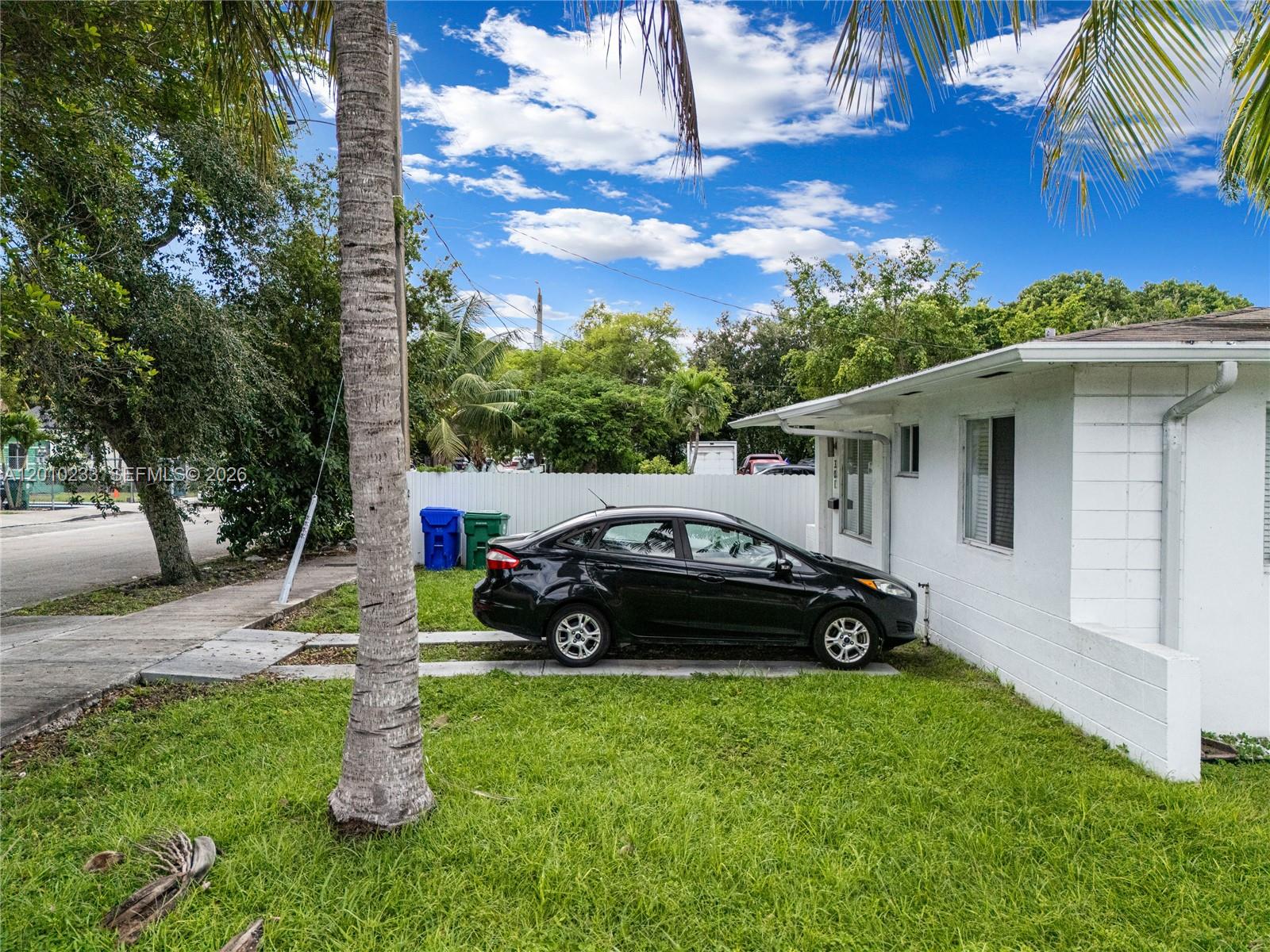 A black sedan is parked on a concrete driveway next to a white house — 301 NW 34th St, Miami FL 33127, MIAMI, FL
