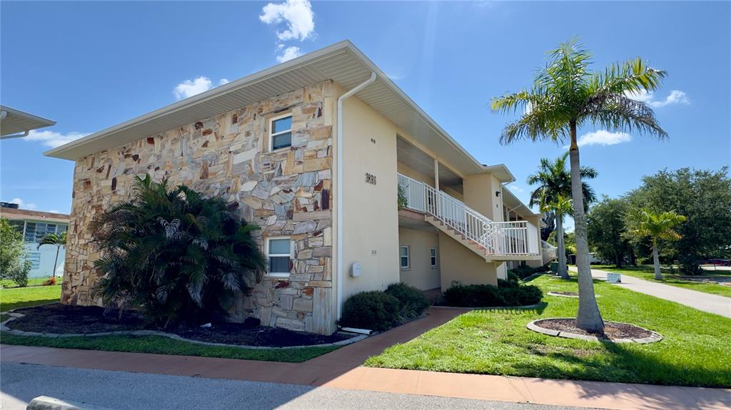A two-story apartment building features a stone facade, a palm tree, and an exterior staircase — 3136 HARBOR BOULEVARD UNIT 2A, PORT CHARLOTTE, FL