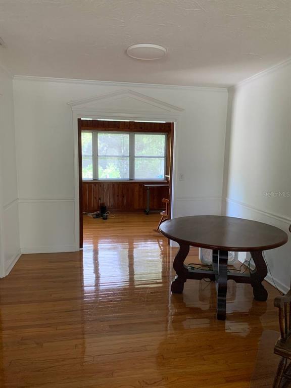 A dining room with hardwood floors leads into a sunroom with wood-paneled walls — 362 FOSTER LANE, BELLEAIR, FL