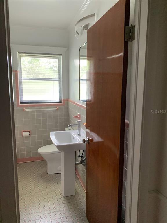 A bathroom features a pedestal sink, a toilet, and light-colored tile walls with pink trim — 362 FOSTER LANE, BELLEAIR, FL