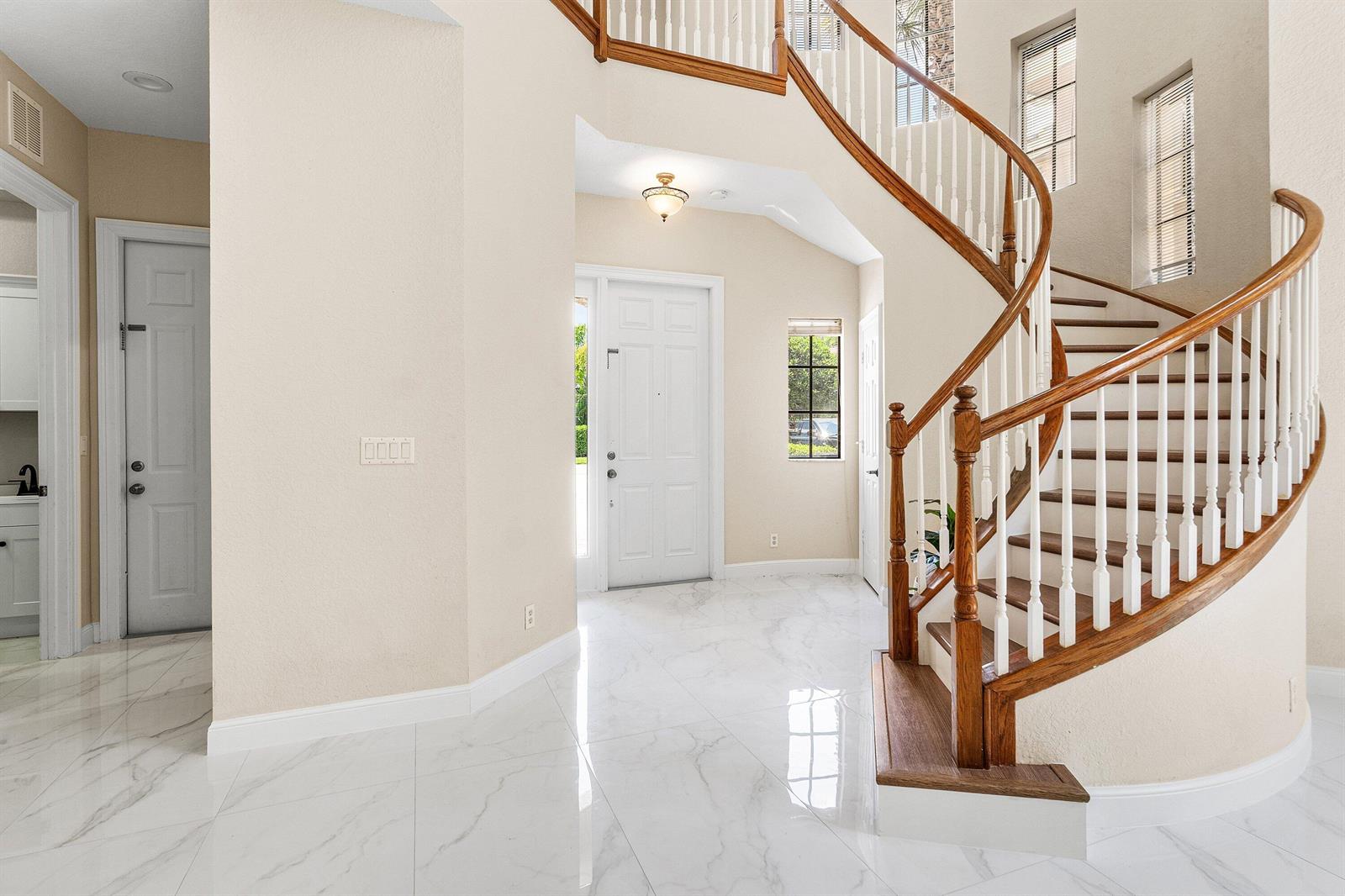 An entryway features white marble floors, a curved wooden staircase, and a white front door — 10293 Medicis Place, Wellington FL 33449, WELLINGTON, FL