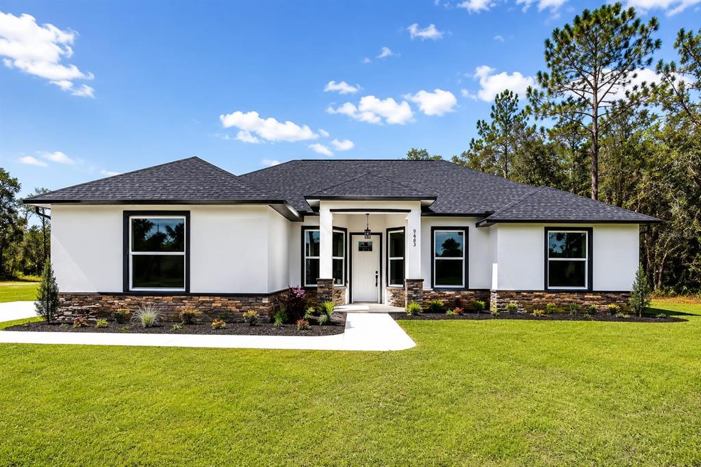 A single-story house with white stucco walls, stone veneer, and a dark shingled roof — 9483 SW 121ST TERRACE, DUNNELLON, FL