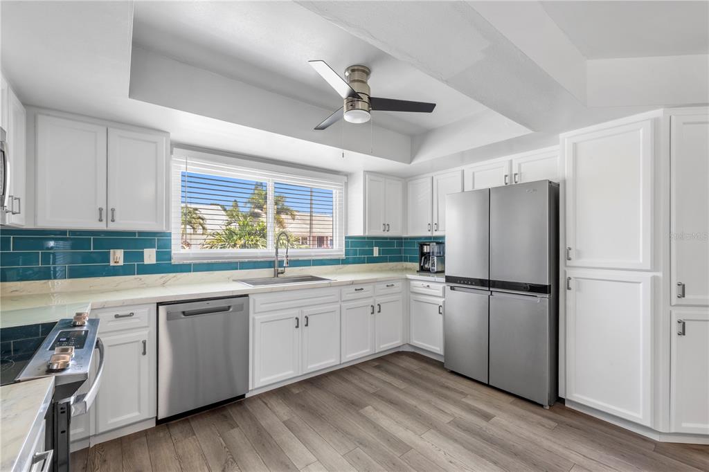 A kitchen features white cabinets, stainless steel appliances, a teal tile backsplash, and wood-look flooring — 3122 WHISPERING DRIVE N, LARGO, FL