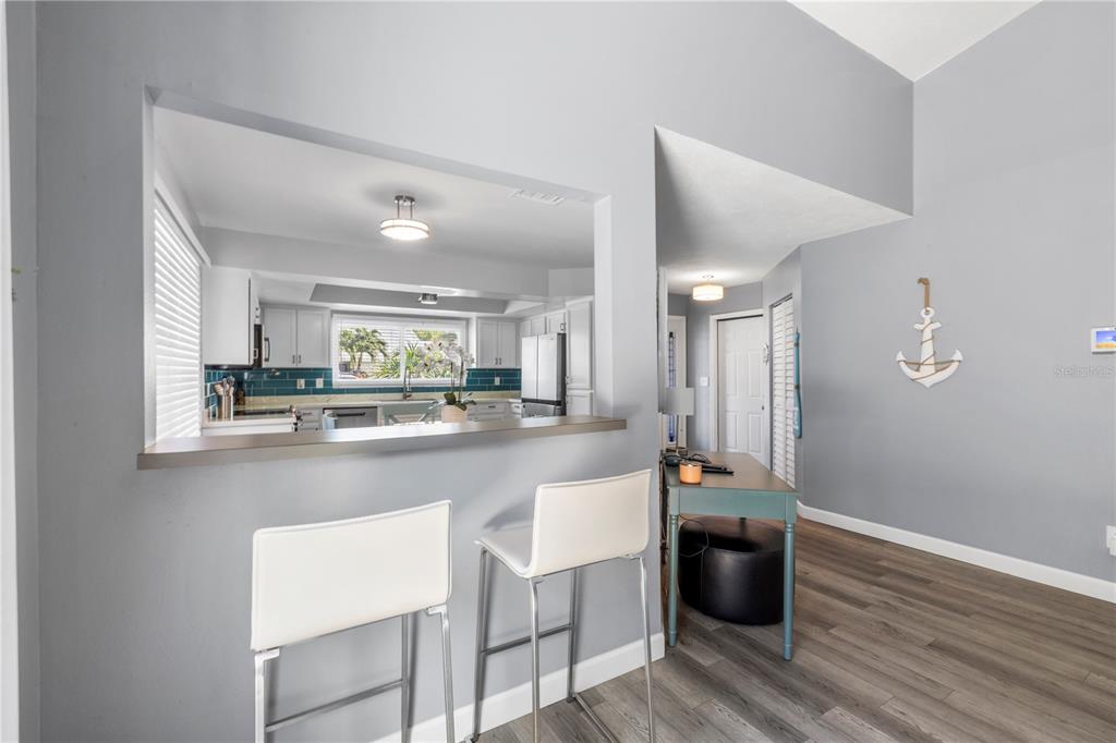 A kitchen with a breakfast bar and stools overlooks a dining area with gray flooring — 3122 WHISPERING DRIVE N, LARGO, FL