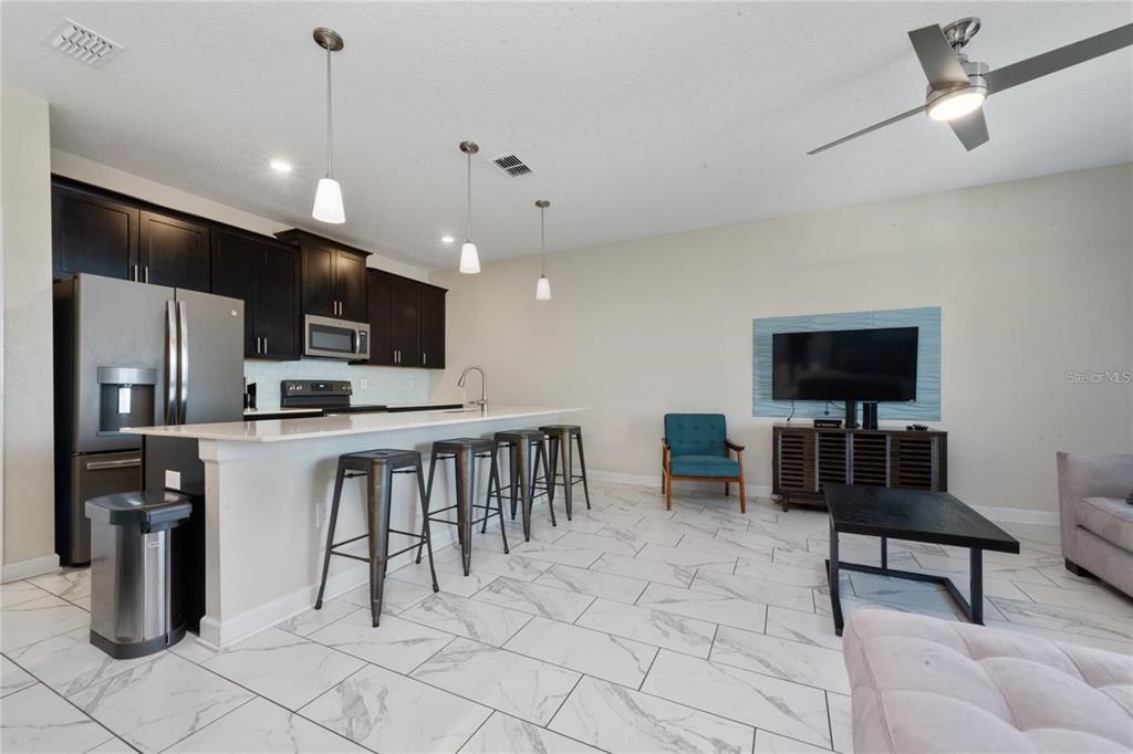 An open-concept kitchen and living area features dark cabinetry, a breakfast bar, and tiled floors — 8932 STINGER DRIVE, DAVENPORT, FL