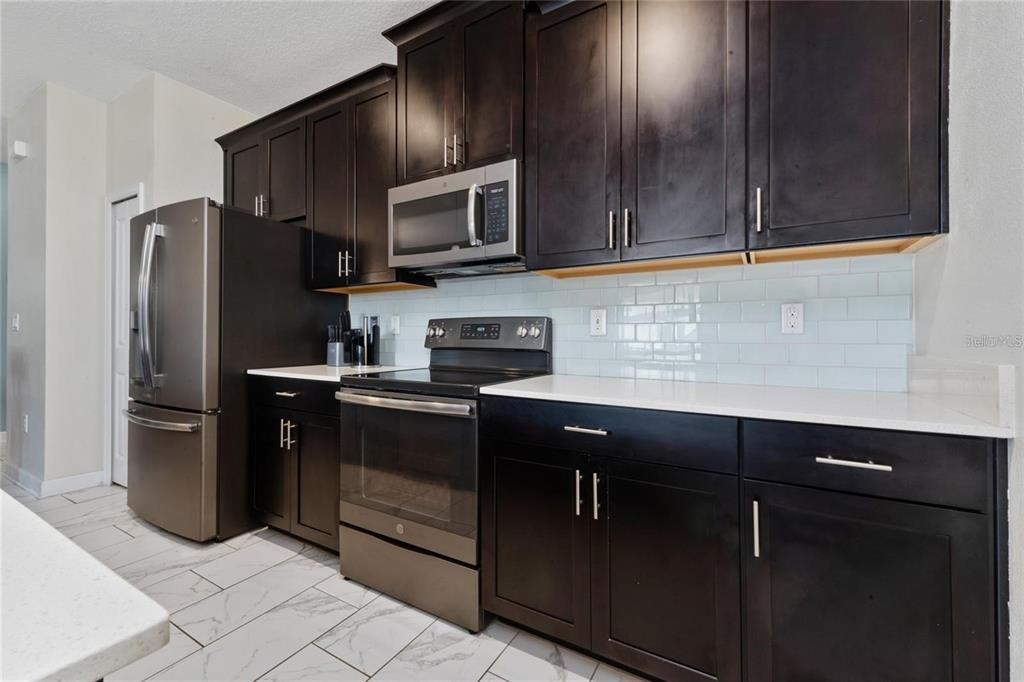 A kitchen features dark wood cabinets, stainless steel appliances, white countertops, and light tile flooring — 8932 STINGER DRIVE, DAVENPORT, FL