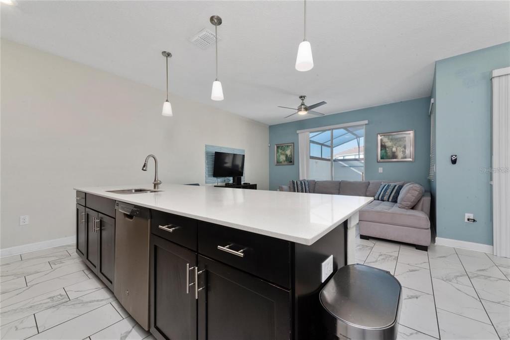 A kitchen island with dark cabinets and a white countertop sits before a living area — 8932 STINGER DRIVE, DAVENPORT, FL