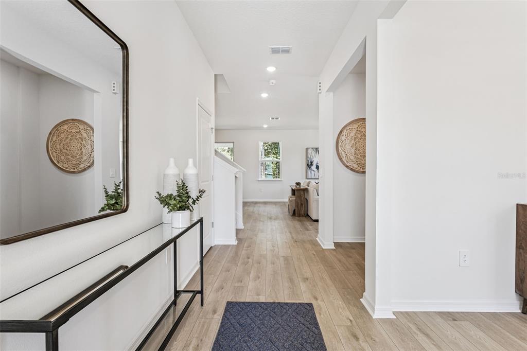 A bright entryway features a glass console table, a mirror, and light wood-look flooring — 4271 DARBY COURT, EUSTIS, FL