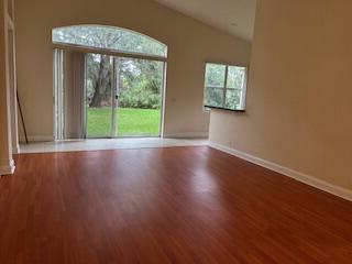An empty living room features wood-look flooring, a vaulted ceiling, and sliding glass doors to outdoors — 6211 Arlington Way, Fort Pierce FL 34951, FORT PIERCE, FL