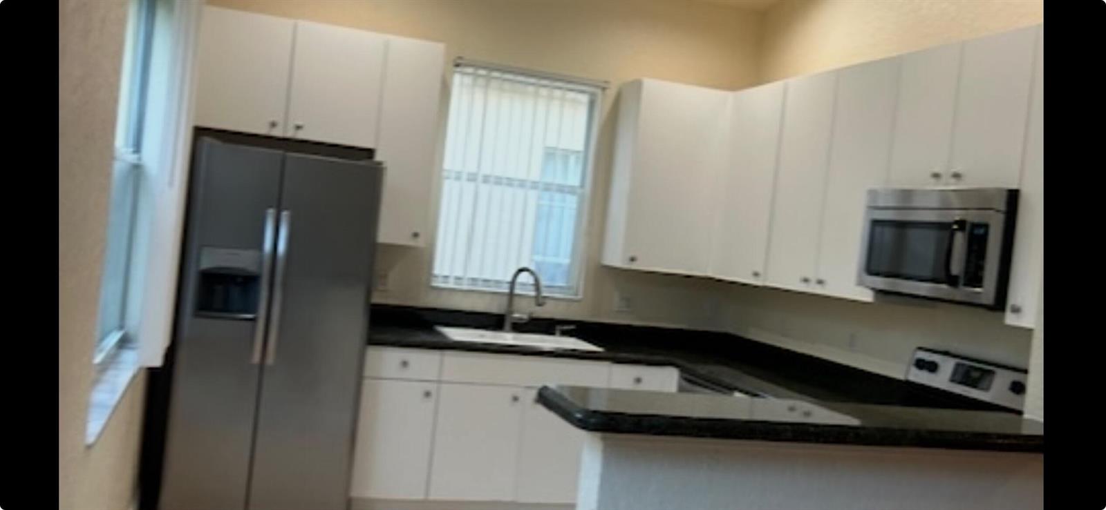 A kitchen features white cabinets, dark countertops, and stainless steel appliances — 6211 Arlington Way, Fort Pierce FL 34951, FORT PIERCE, FL