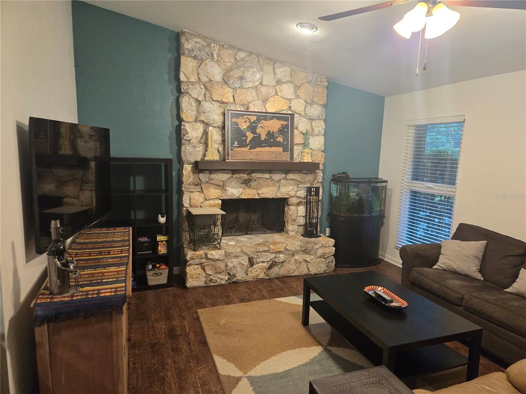 A living room features a stone fireplace, dark wood flooring, and teal accent walls — 7605 SW 7TH PLACE, GAINESVILLE, FL