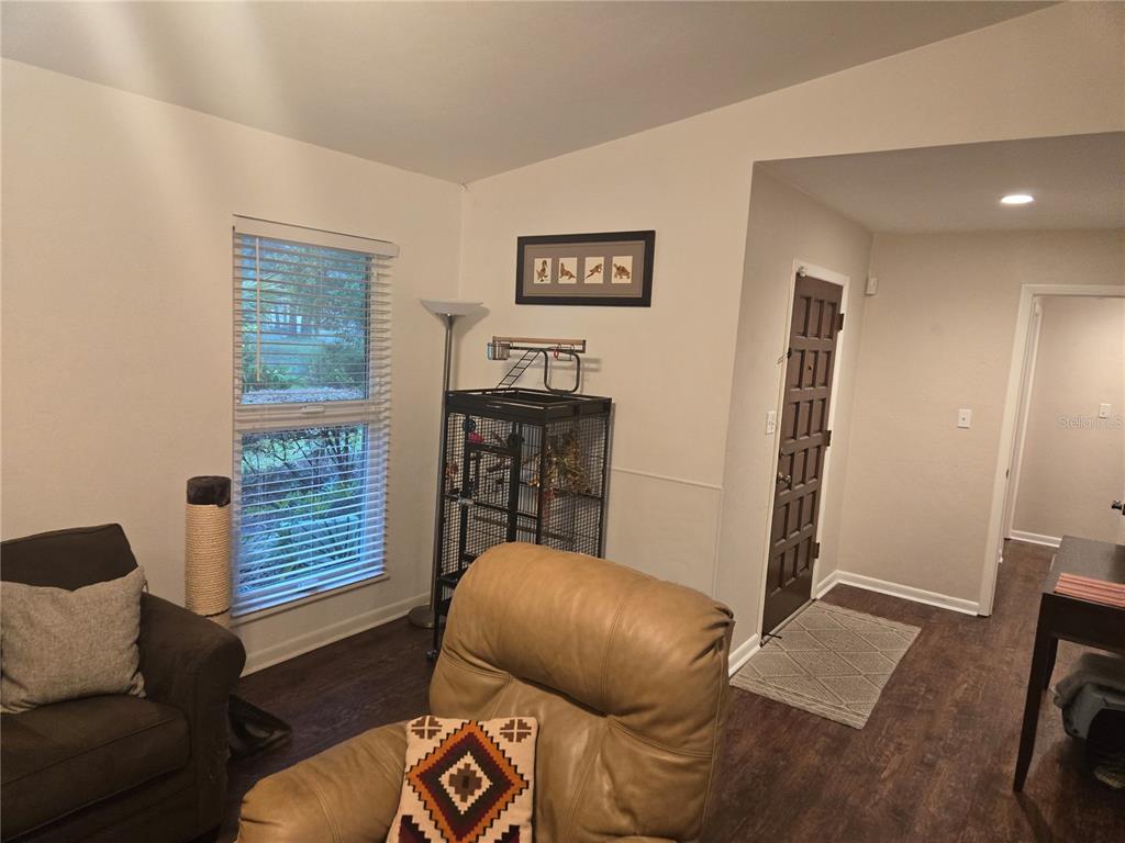 A living room features a tan leather recliner, a dark armchair, and a birdcage near a window — 7605 SW 7TH PLACE, GAINESVILLE, FL