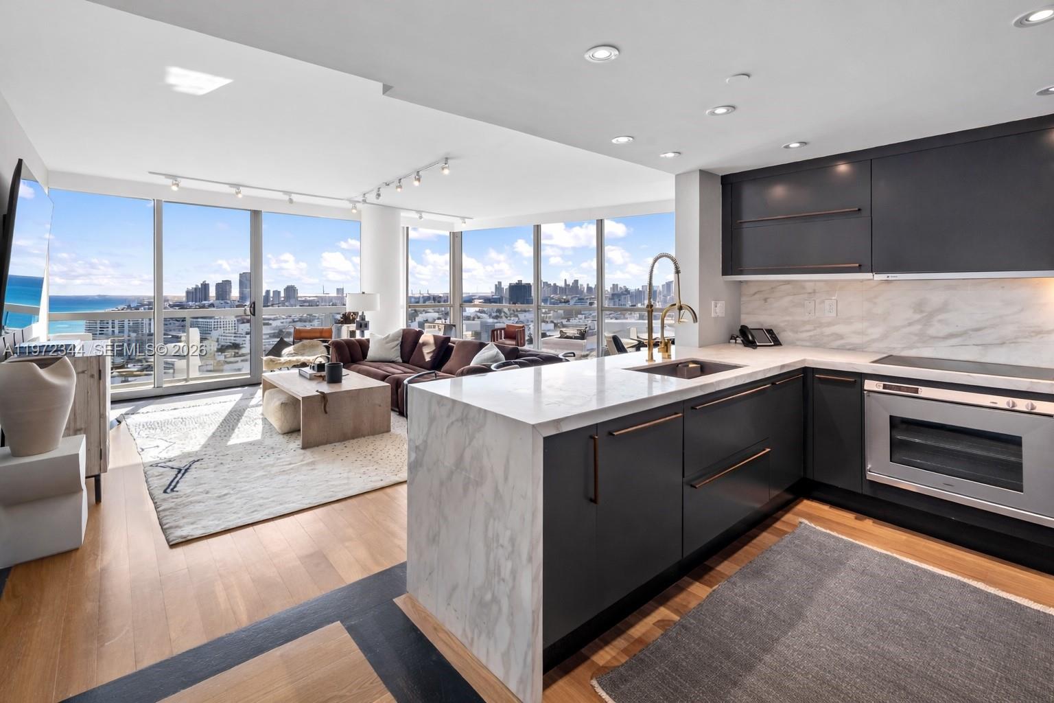 A modern kitchen with dark cabinetry and marble countertops overlooks a living area with city views — 101 20th St # 2706, Miami Beach FL 33139, MIAMI BEACH, FL
