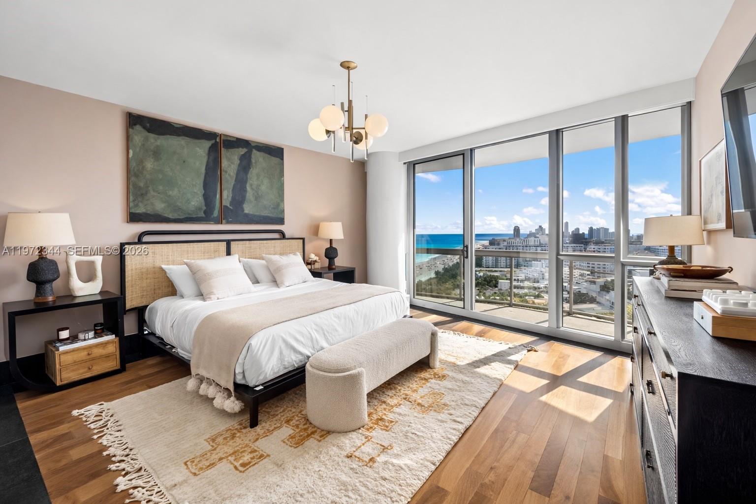 A bedroom features a bed with a rattan headboard, a chandelier, and floor-to-ceiling ocean views — 101 20th St # 2706, Miami Beach FL 33139, MIAMI BEACH, FL