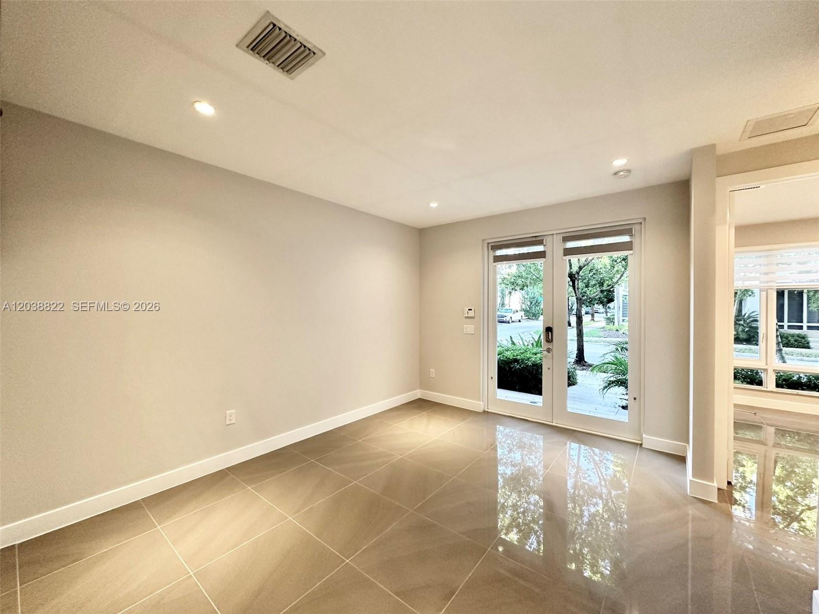 An empty room features large beige floor tiles, light gray walls, and glass double doors — 10560 NW 63rd Ter, Doral FL 33178, DORAL, FL