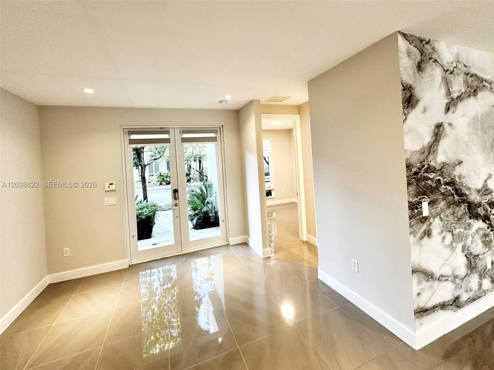 A room with glossy tile floors, a marble-patterned accent wall, and double glass doors — 10560 NW 63rd Ter, Doral FL 33178, DORAL, FL