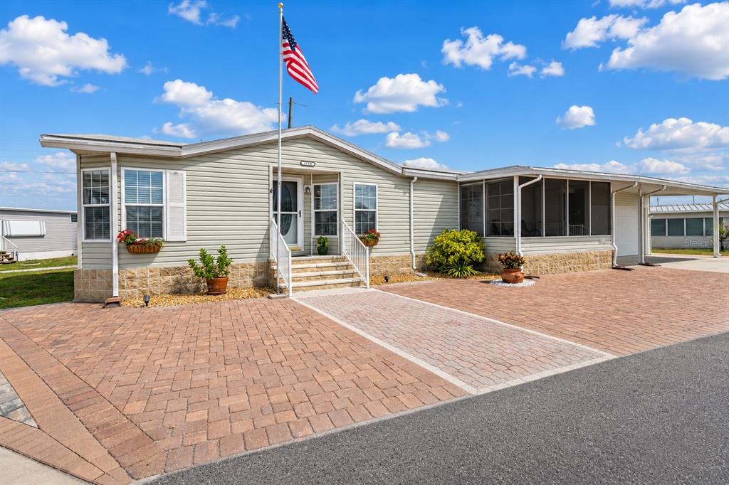 A light-colored manufactured home features a brick paver driveway, a screened porch, and an American flag — 1710 INDIANA AVENUE, BRADENTON, FL