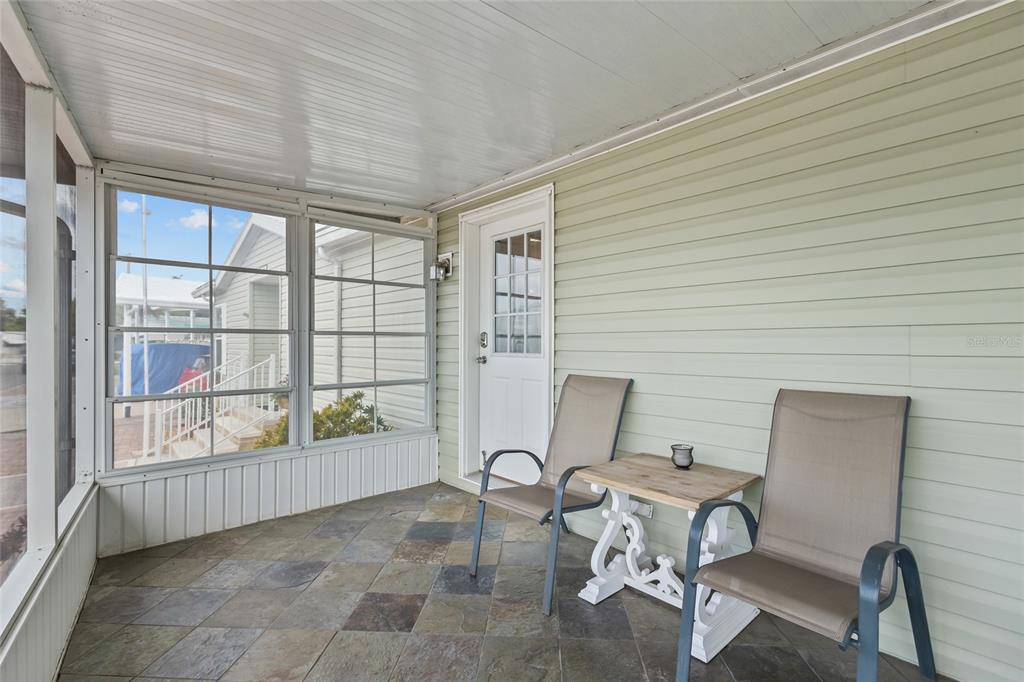 A screened-in porch features light green siding, a tiled floor, and two chairs with a table — 1710 INDIANA AVENUE, BRADENTON, FL