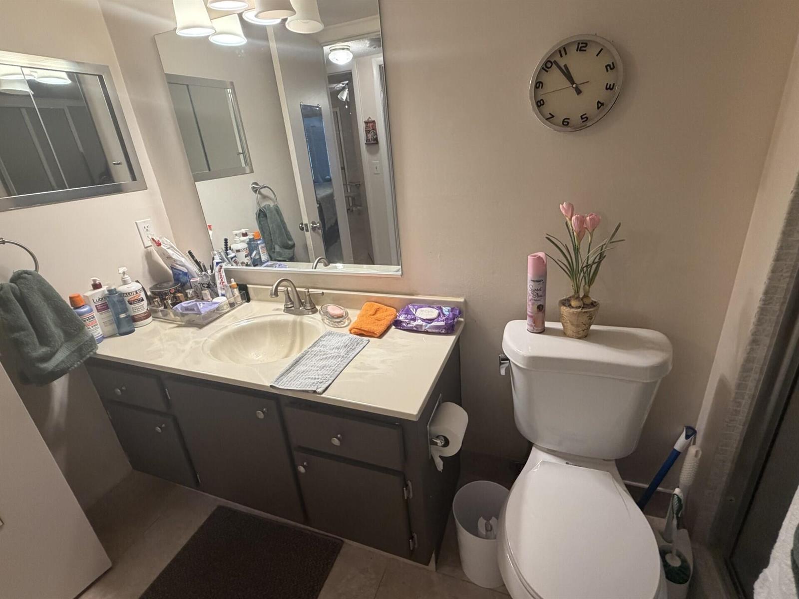 A bathroom features a dark vanity with a light countertop, a toilet, and a wall clock — 1011 Ventnor Crescent, Deerfield Beach FL 33442, DEERFIELD BEACH, FL