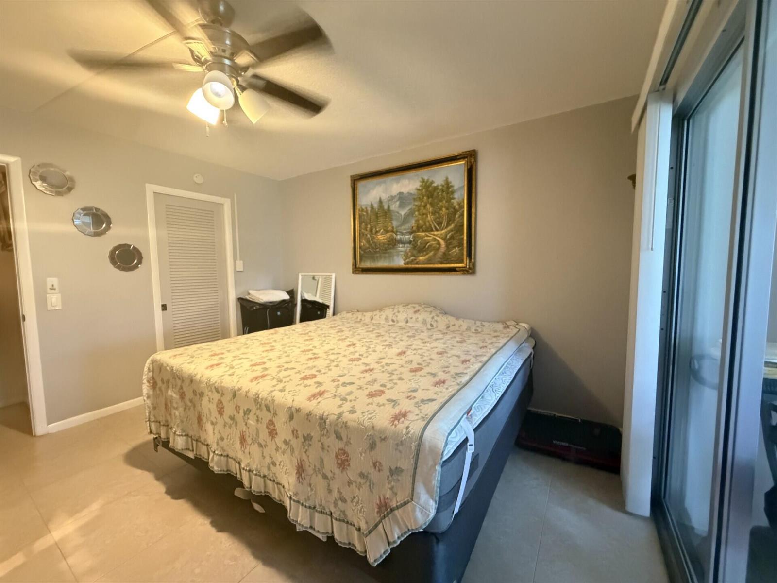 A bedroom features a bed with a floral coverlet, a ceiling fan, and wall art — 1011 Ventnor Crescent, Deerfield Beach FL 33442, DEERFIELD BEACH, FL