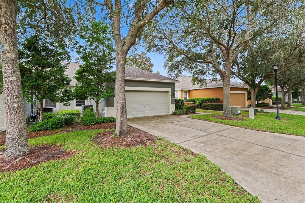 A concrete driveway leads to the garage of a single-story house shaded by large trees — 13703 CREST LAKE DRIVE, HUDSON, FL